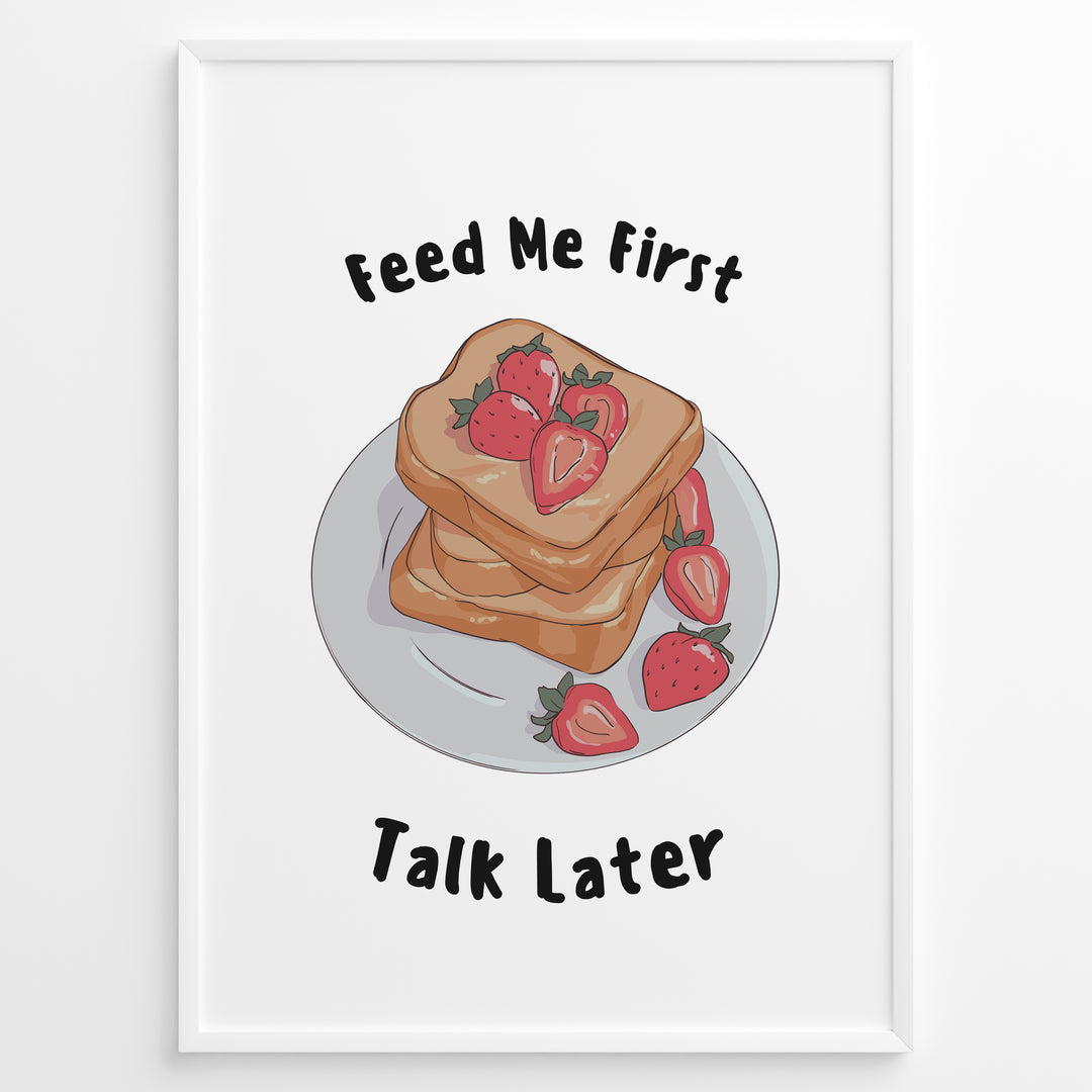 Funny kitchen poster with a plate of toast and strawberries, and the text “Feed Me First Talk Later,” framed in black on a white background.