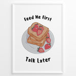 Load image into Gallery viewer, Funny kitchen poster with a plate of toast and strawberries, and the text “Feed Me First Talk Later,” framed in black on a white background.
