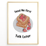 Load image into Gallery viewer, Funny kitchen poster with a plate of toast and strawberries, and the text “Feed Me First Talk Later,” framed in black on a white background.
