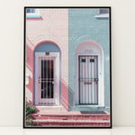 Load image into Gallery viewer, Plakat med farverige døre | Sommer og Strand Plakater | Denne plakat viser en pink og en blå dør side om side, hver i en buet dørkarm, på en farverig bygning. Perfekt til dem, der elsker unik arkitektur.
