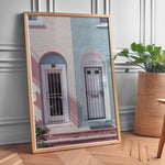 Load image into Gallery viewer, Plakat med farverige døre | Sommer og Strand Plakater | Denne plakat viser en pink og en blå dør side om side, hver i en buet dørkarm, på en farverig bygning. Perfekt til dem, der elsker unik arkitektur.
