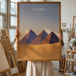 Load image into Gallery viewer, Cairo Vintage Travel Plakat | Vintage Travel Poster | Denne plakat viser de ikoniske Giza-pyramider i Cairo, Egypten, mod en gradient himmel og et ørkenlandskab.
