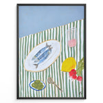 Load image into Gallery viewer, Mediterranean still life poster with fish on a white plate, lemon, radishes, olives, and a pink drink on a green and white striped tablecloth, framed as kitchen wall art.
