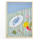 Load image into Gallery viewer, Mediterranean still life poster with fish on a white plate, lemon, radishes, olives, and a pink drink on a green and white striped tablecloth, framed as kitchen wall art.
