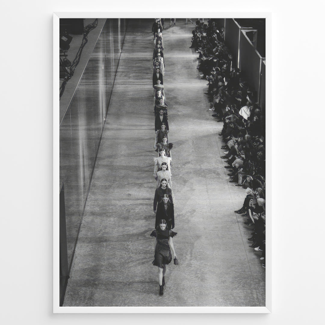Fashion Plakat | Black & White Fashion Runway – Editorial Wall Art Print Plakaty.dk | Black and white photograph of runway models walking in a single-file line during a fashion show, with seated spectators on one side of the runway.