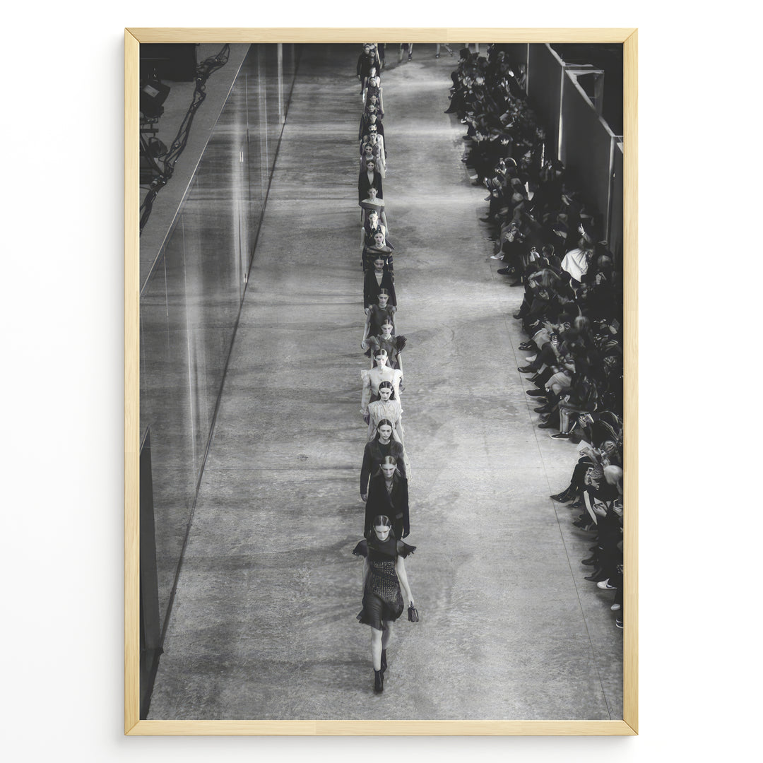 Fashion Plakat | Black & White Fashion Runway – Editorial Wall Art Print Plakaty.dk | Black and white photograph of runway models walking in a single-file line during a fashion show, with seated spectators on one side of the runway.