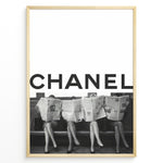 Load image into Gallery viewer, Fashion Plakat | CHANEL Newspaper Bench – Fashion Art Poster Plakaty.dk | Black and white fashion poster of four women sitting on a bench reading newspapers, with the bold text &quot;CHANEL&quot; across the top half of the image.
