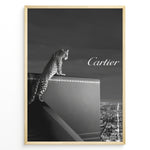 Load image into Gallery viewer, Fashion Plakat | Cartier Panther Over the City: Iconic Elegance in Monochrome Plakaty.dk | Black and white image of a panther perched on a Cartier box overlooking a city skyline at night, with the Cartier logo in the sky.
