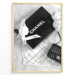 Load image into Gallery viewer, Fashion Plakat | Chanel Gift Box &amp; Handbag Flatlay Wall Art Plakaty.dk | Black and white flatlay of a Chanel gift box with ribbon, camellia flowers, and a quilted Chanel handbag on a soft surface.
