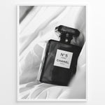 Load image into Gallery viewer, Fashion Plakat | Chanel No. 5 L’Eau Perfume Bottle – Black and White Fashion Photography Plakaty.dk | Black and white photo of a Chanel No. 5 L’Eau perfume bottle resting on a bed of soft white fabric.
