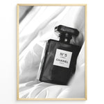 Load image into Gallery viewer, Fashion Plakat | Chanel No. 5 L’Eau Perfume Bottle – Black and White Fashion Photography Plakaty.dk | Black and white photo of a Chanel No. 5 L’Eau perfume bottle resting on a bed of soft white fabric.
