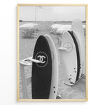 Load image into Gallery viewer, Fashion Plakat | Chanel Surfboards on the Beach – Luxury Meets Coastal Lifestyle in Black and White Plakaty.dk | Black and white photo of Chanel and J12 Yacht Club surfboards on a sandy beach with umbrellas and lounge chairs in the background
