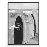Load image into Gallery viewer, Fashion Plakat | Chanel Surfboards on the Beach – Luxury Meets Coastal Lifestyle in Black and White Plakaty.dk | Black and white photo of Chanel and J12 Yacht Club surfboards on a sandy beach with umbrellas and lounge chairs in the background
