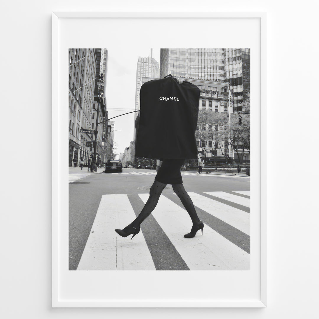 Fashion Plakat | Chic Chanel Street Style Fashion Print Plakaty.dk | Black and white photo of a stylish woman in heels crossing a city street while carrying a Chanel garment bag, framed as wall art.