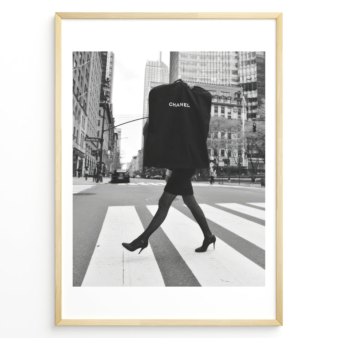 Fashion Plakat | Chic Chanel Street Style Fashion Print Plakaty.dk | Black and white photo of a stylish woman in heels crossing a city street while carrying a Chanel garment bag, framed as wall art.