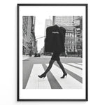 Load image into Gallery viewer, Fashion Plakat | Chic Chanel Street Style Fashion Print Plakaty.dk | Black and white photo of a stylish woman in heels crossing a city street while carrying a Chanel garment bag, framed as wall art.
