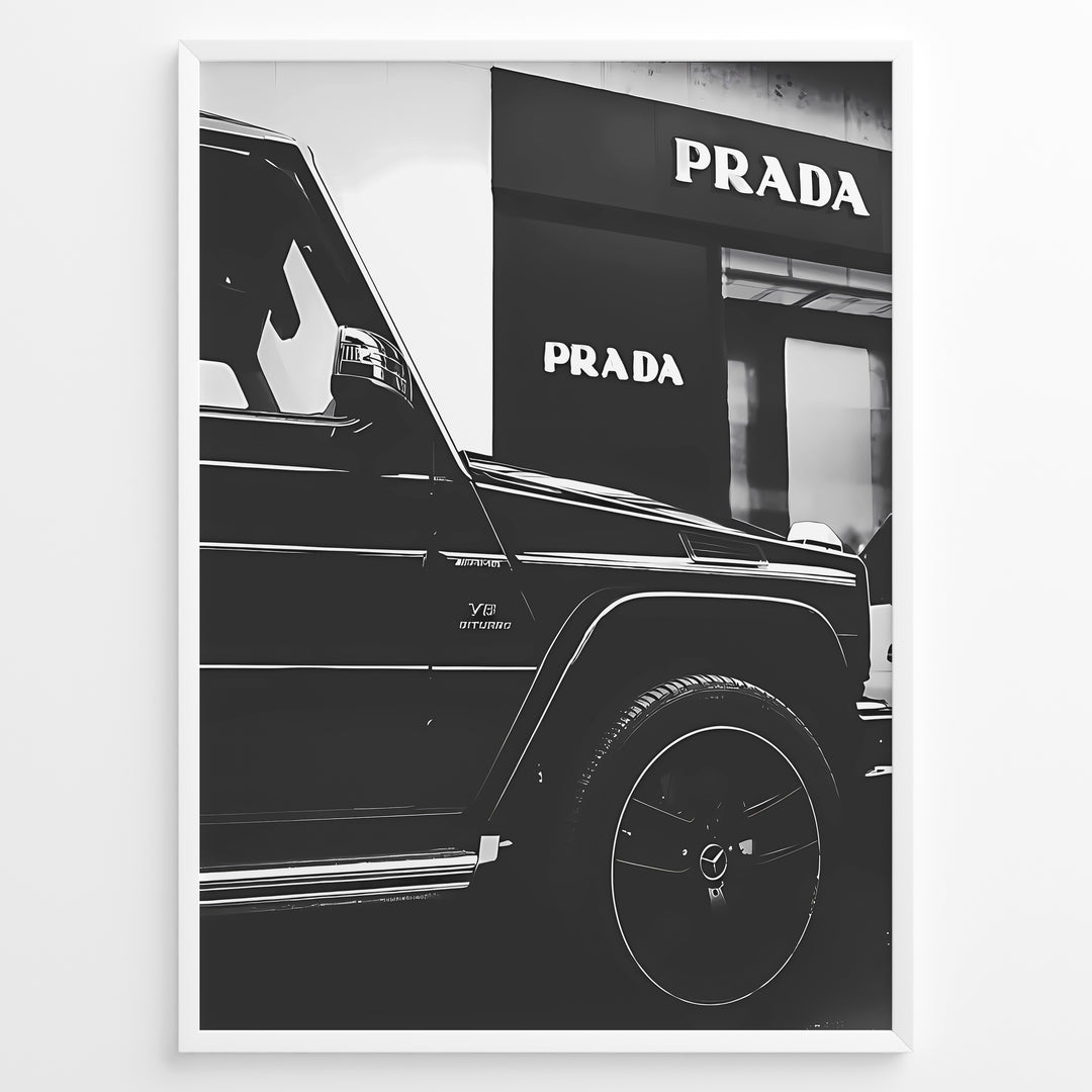 Fashion Plakat | Mercedes-Benz G-Wagon and Prada Store Black and White Art Print Plakaty.dk | A framed, black and white photograph showing the side profile of a Mercedes-Benz G-Wagon AMG parked in front of a Prada store. The car's V8 BITURBO badge is visible, and the Prada logo is prominent on the building's facade.