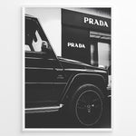 Load image into Gallery viewer, Fashion Plakat | Mercedes-Benz G-Wagon and Prada Store Black and White Art Print Plakaty.dk | A framed, black and white photograph showing the side profile of a Mercedes-Benz G-Wagon AMG parked in front of a Prada store. The car&#39;s V8 BITURBO badge is visible, and the Prada logo is prominent on the building&#39;s facade.

