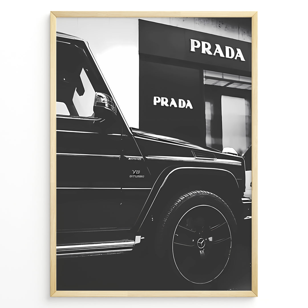 Fashion Plakat | Mercedes-Benz G-Wagon and Prada Store Black and White Art Print Plakaty.dk | A framed, black and white photograph showing the side profile of a Mercedes-Benz G-Wagon AMG parked in front of a Prada store. The car's V8 BITURBO badge is visible, and the Prada logo is prominent on the building's facade.