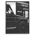 Load image into Gallery viewer, Fashion Plakat | Mercedes-Benz G-Wagon and Prada Store Black and White Art Print Plakaty.dk | A framed, black and white photograph showing the side profile of a Mercedes-Benz G-Wagon AMG parked in front of a Prada store. The car&#39;s V8 BITURBO badge is visible, and the Prada logo is prominent on the building&#39;s facade.
