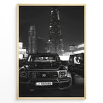 Load image into Gallery viewer, Fashion Plakat | Midnight Luxury – Brabus G-Wagon in Dubai Plakaty.dk | Black and white photo of a Brabus G-Wagon parked in front of the Dubai skyline at night, with skyscrapers like Burj Khalifa and EMAAR towers in the background.
