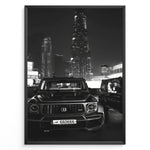 Load image into Gallery viewer, Fashion Plakat | Midnight Luxury – Brabus G-Wagon in Dubai Plakaty.dk | Black and white photo of a Brabus G-Wagon parked in front of the Dubai skyline at night, with skyscrapers like Burj Khalifa and EMAAR towers in the background.
