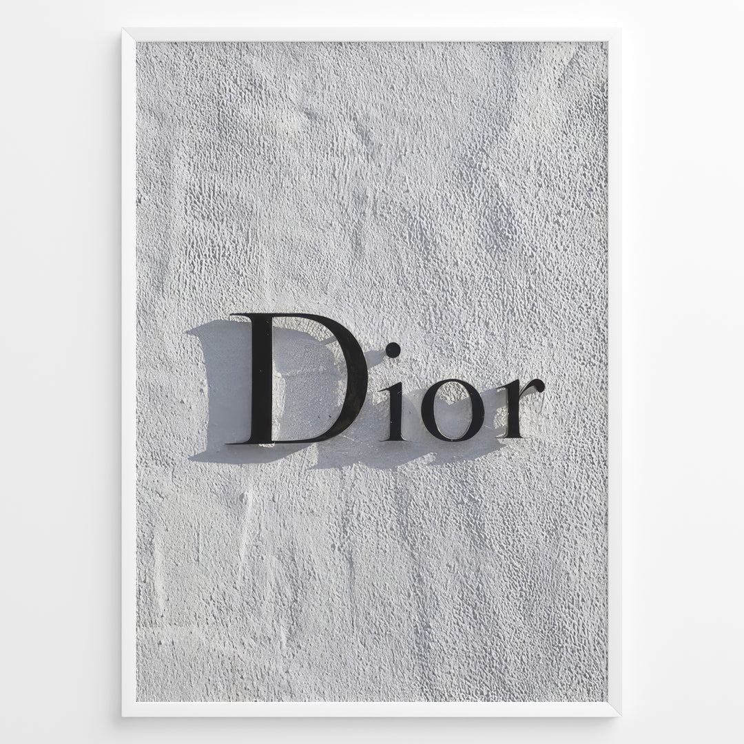 Fashion Plakat | Minimalist Dior Wall Sign – Timeless Fashion Statement Plakaty.dk | Minimalist black Dior logo mounted on a textured white wall, casting a soft shadow and evoking luxury and elegance.