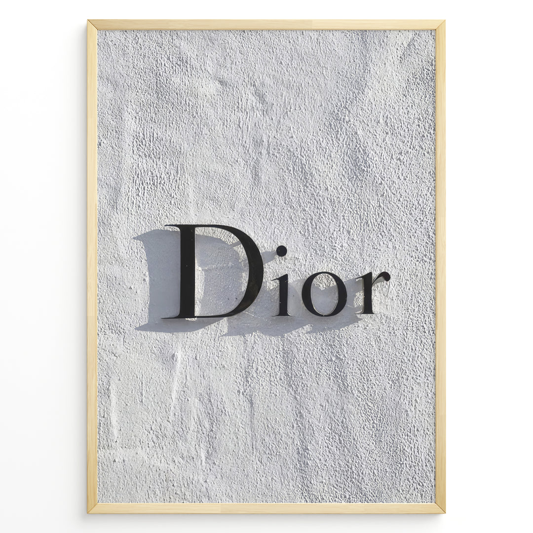 Fashion Plakat | Minimalist Dior Wall Sign – Timeless Fashion Statement Plakaty.dk | Minimalist black Dior logo mounted on a textured white wall, casting a soft shadow and evoking luxury and elegance.