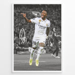 Load image into Gallery viewer, Framed plakat of Vinícius Jr. in a Real Madrid kit celebrating with a pointing gesture, color-highlighted against a black and white background with signature
