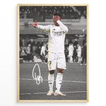 Load image into Gallery viewer, Framed plakat of Vinícius Jr. in a Real Madrid kit doing an eye-cover celebration, with a black and white background and printed signature
