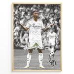 Load image into Gallery viewer, Framed Plakat of Vinícius Jr. in a Real Madrid kit doing a shrug celebration, with a black and white background and visible signature
