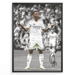 Load image into Gallery viewer, Framed Plakat of Vinícius Jr. in a Real Madrid kit doing a shrug celebration, with a black and white background and visible signature
